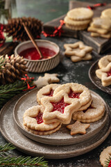 Homemade Linzer Christmas cookies filled with raspberry jam and dusted with sugar on ceramic plate with fir tree branches and festive decorations