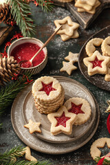 Homemade Linzer Christmas cookies filled with raspberry jam and dusted with sugar on ceramic plate with fir tree branches on wooden table