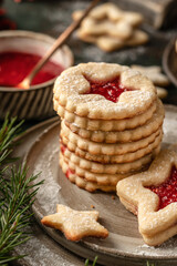 Stack of Homemade Linzer Christmas cookies filled with raspberry jam and dusted with sugar on ceramic plate close up with fir tree branches