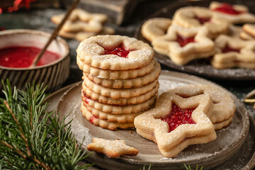 Stack of Homemade Linzer Christmas cookies filled with raspberry jam and dusted with sugar on ceramic plate close up with fir tree branches