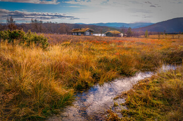 Traditional Nordic cabins in autumn tundra landscape with stream