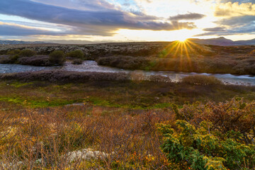 Autumn tundra river with sunburst and mountains