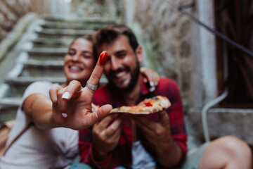 Close up of a young couple eating pizza outside, dipping finger in tomato sauce.