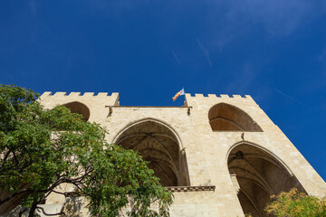 The Serranos Towers Torres de Serranos stand tall in a sunlit plaza in Valencia. Massive Gothic gateway, which features grand vaulted arches and a flag flying from its crenelated top.