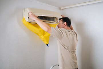 Technician standing on ladder and attaching waterproof bag to air conditioner, preparing for cleaning and maintenance to ensure optimal cooling performance. Concept of air condition service.