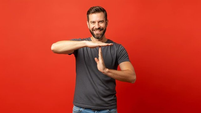 Cheerful man demonstrating timeout gesture against vibrant red background for communication concept