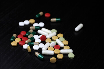 Pills and capsules scattered on a black wooden table. Background for pharmacy, antibiotics, vitamins, dietary supplements