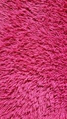 Close-up of a vibrant pink shaggy carpet texture with long, soft fibers creating a cozy and warm...