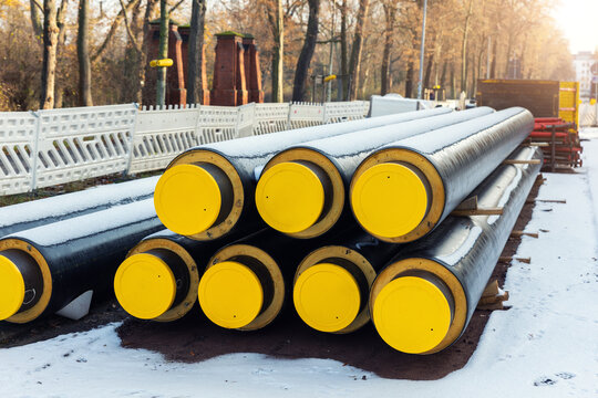 Insulated district heating pipes stacked urban construction site winter covered snow installation public utility network. Energy infrastructure pipeline thermal insulation municipal heating supply