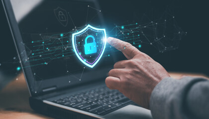 Digital cybersecurity concept. Hand interacting with a glowing shield and lock icon over a laptop. Representing data protection, network security, privacy, encryption and secure online technology.