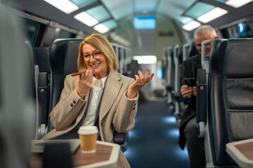 Mature businesswoman sending voice message while traveling on modern train