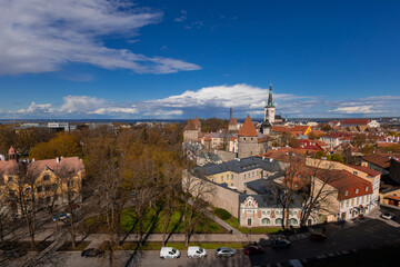 Wiide panoramic view of Tallinn, capturing the contrast between the lush parks of the lower town and the red-tiled roofs and defensive towers of the historic Old Town under a dramatic, cloud-filled