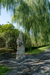 Fototapeta premium Side view of a stone guardian warrior statue on the Ming Tombs Sacred Way under green willow branches.