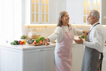 Happy senior couple dancing while cooking in kitchen