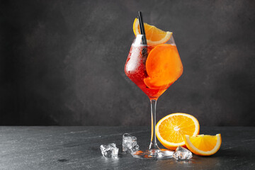 Glass of refreshing spritzer cocktail, ice cubes and orange slices on black table. Space for text