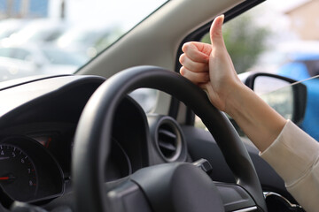 Positive Driving Gesture Inside Car. The hand shows the gesture super, cool, good, thumbs up on the steering wheel of the car.