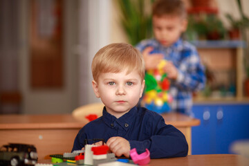 Focused Child Builds With Colorful Blocks in a Vibrant Classroom Setting While Another Child Plays in the Background © malyutinaanna