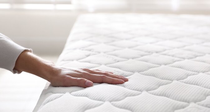 Woman touching soft mattress on bed indoors, closeup