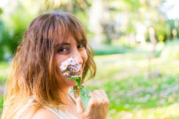 Profile portrait of a woman smiling and looking at the camera while holding a small bouquet of flowers. © Carbonero Stock