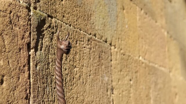 Wrought iron dragon head ring on an ancient stone wall. Close-up view of an antique wrought iron mooring ring with a dragon-shaped head, meticulously handcrafted and affixed to a sunlit, stone wall