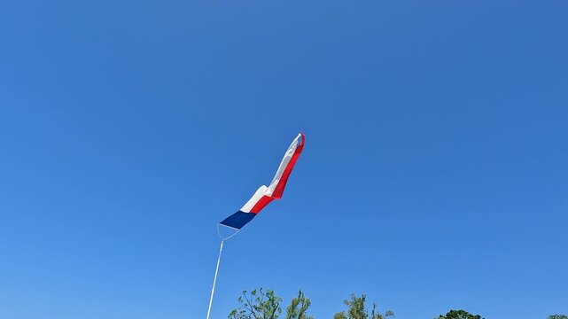 Nautical red, white and blue patriotic triangle shaped pennant flag waves in the wind, set against a clear blue sky. The flags are used for decoration, as well as a deterrent for birds.