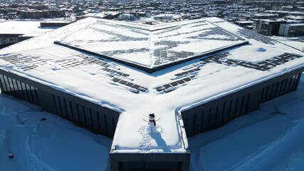 Lone snowman adorns a snow-covered modern building rooftop under a bright sky