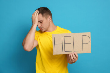 Worried man holding sign with word Help on light blue background