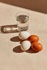Still life with water glass and four eggs, stark shadows on a neutral surface