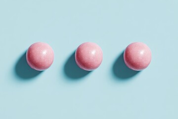 Three pink candies aligned on a pastel blue background, top-down view