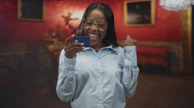 Woman holding creditcard with thumb up gesture, smiling at card in museum building interior; celebration success.