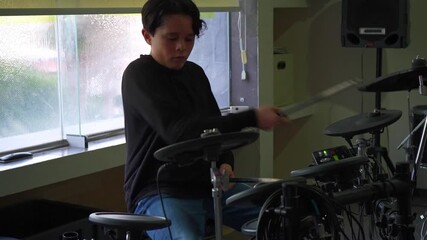 Young music student playing with deep concentration at the electronic drum kit, focused expression and precise movements. Individual music practice, discipline, learning rhythm and percussion skills