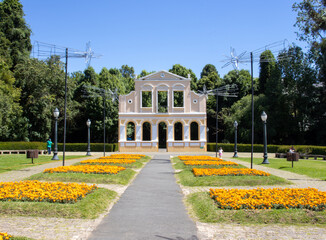 Obraz premium Front facade of the Bosque Alemão located in Curitiba, Paraná, Brazil. The structure features German-inspired architecture with arches, symmetry, and light tones, surrounded by green areas in an urban