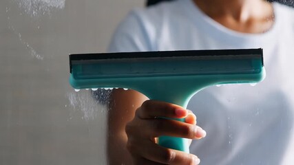 Young woman using professional rubber squeegee to clean soapy glass surface representing domestic housework and window washing