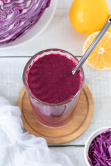 Red cabbage smoothie in a glass on wooden kitchen table. Healthy homemade detox blended drink.
