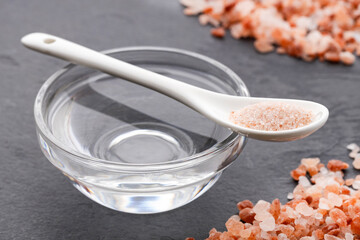 Himalayan pink salt next to a clear container of water on a dark slate surface