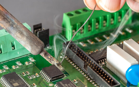 Close up of hand soldering electronic components on PCB printed circuit board with soldering iron and solder wire. - Powered by Adobe