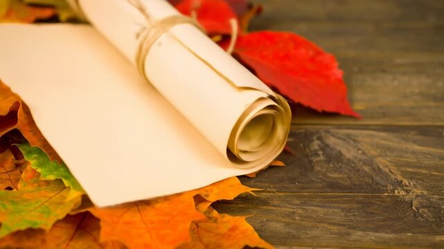 A scroll with twine, resting on autumn leaves, with a wooden background.