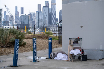 Items and belongings associated with homelessness, including a shopping trolley and bedding, beneath the Bolte Bridge, in Melbourne&rsquo;s Docklands in Australia, against concrete infrastructure and city