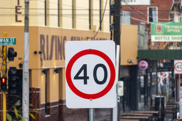 A 40 km/h speed limit road sign stands on a suburban street in Melbourne, Australia, with shopfronts a commercial street in the background. Concept of local traffic regulation, urban street safety