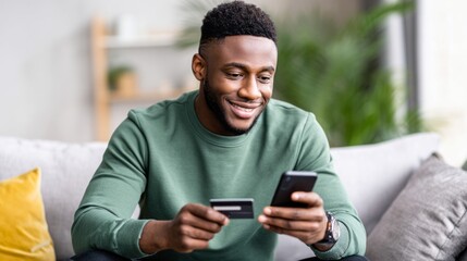 Black man using cell phone and banking card for m commerce from sofa, shopping online, experiencing easy digital transaction. Shopping in a store