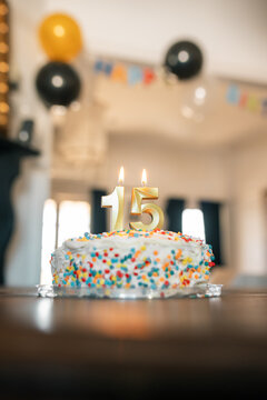 Lit gold 15 candles on birthday cake in decorated dining room with balloons and bunting