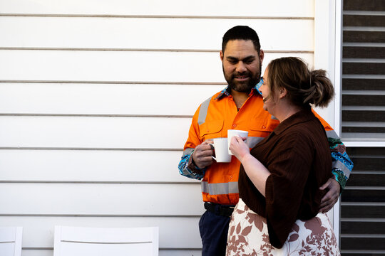 Mixed ethnicity couple having a cup of coffee outside a white weatherboard house