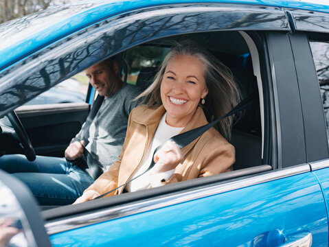 Man and woman fastening seatbelt inside blue car