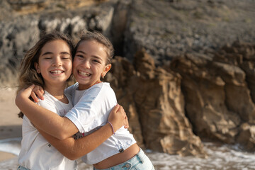 Happy girls hugging each other on beach near sea smiling and enjoying fun summer vacation together during sunny day