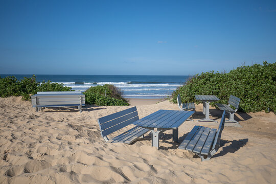 Aftermath of coastal storms with picnic tables and chairs buried in sand along the beach