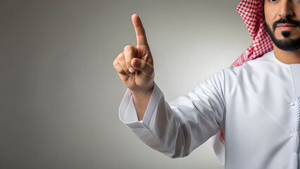 Close-up of a Middle Eastern man in traditional white thawb and red-and-white ghutra pointing upwards with index finger.