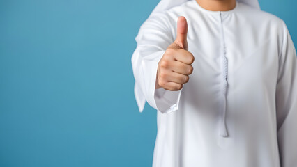 A person in traditional white thawb garment gives a thumbs-up gesture on a blue background.