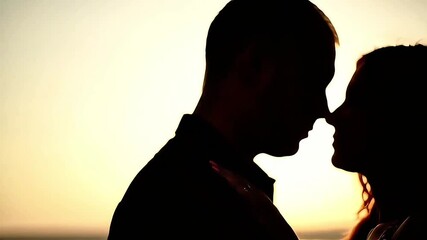 Silhouette of a romantic couple sharing a tender moment on Valentine's Day against a warm, golden sunset background.