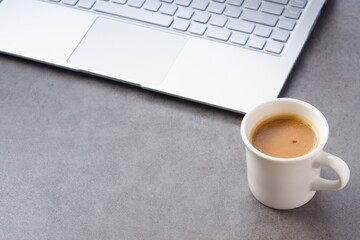 パソコンとコーヒー - 淹れたてのコーヒーを飲みながら、ノートパソコンでデスクワーク中のイメージ
