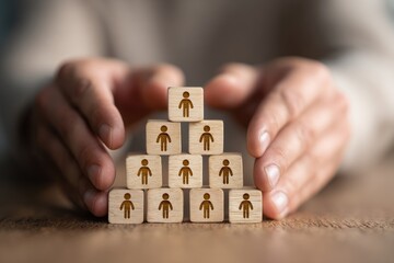 Hands protect wooden blocks forming a human hierarchy pyramid structure.